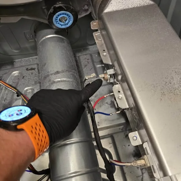 Gloved technician pointing to dryer thermal fuse and thermostat on blower chute in Cambridge MA